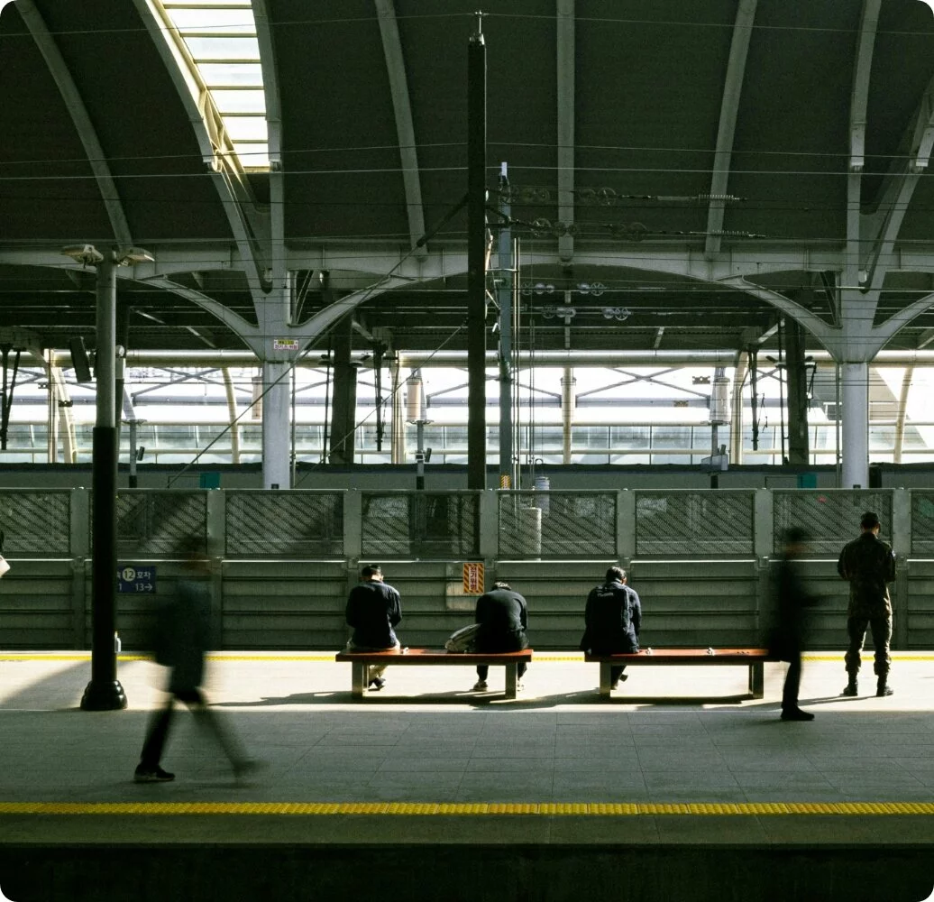 A train stop with commuters waiting on a bench and walking by