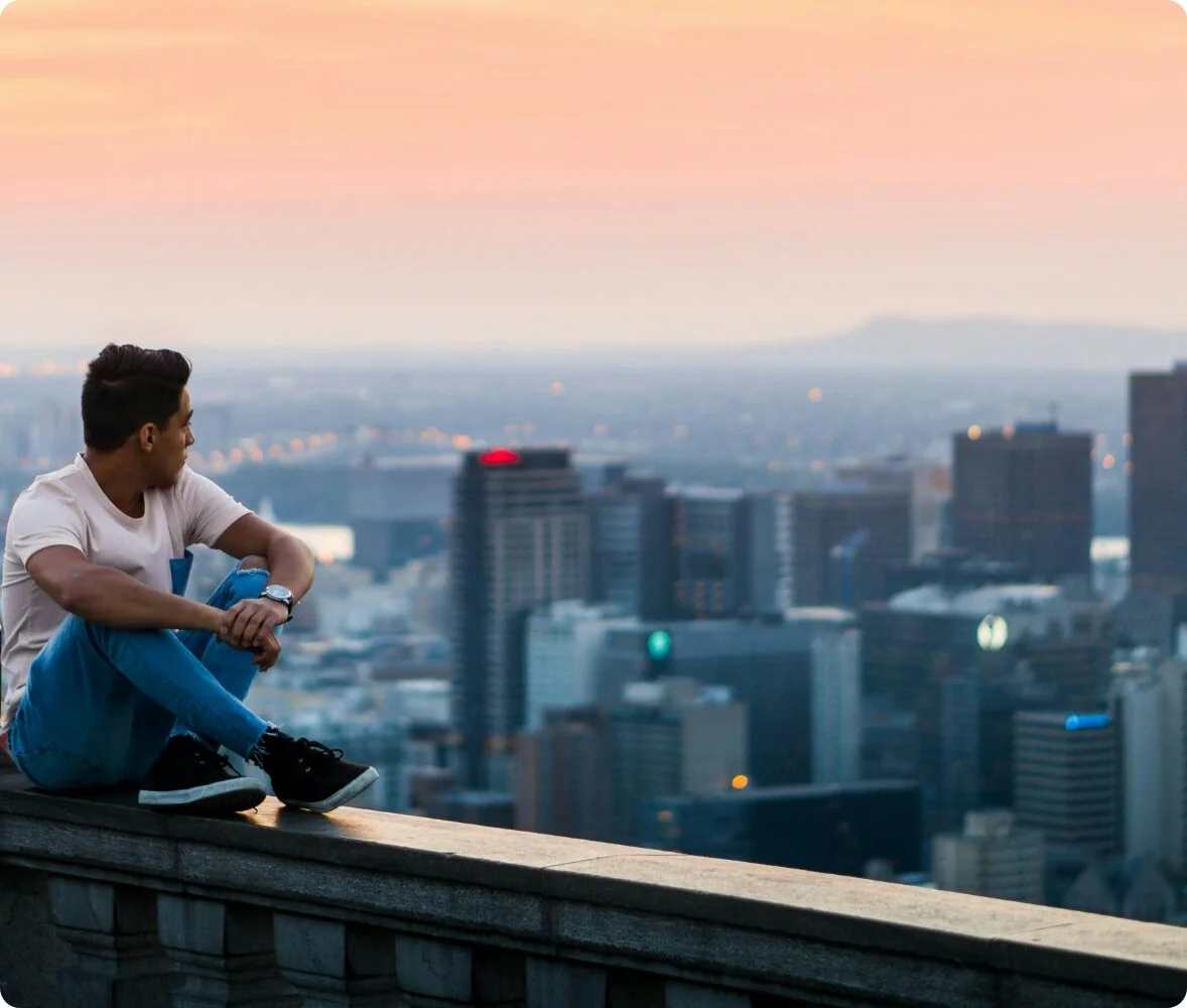 A man sitting on a balcony looking over a city lit by the sunset