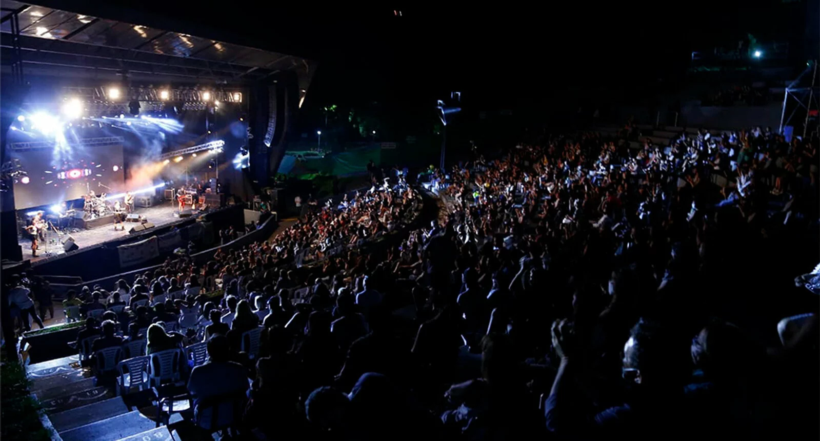 A crowd of people enjoy music in the summer in the dark at the amphitheater