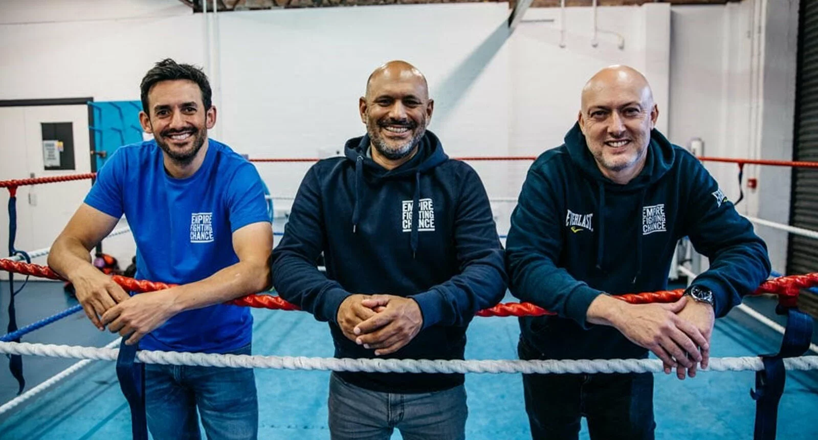 Three Empire Fighting Chance boxing club staff smile for the camera posed inside of the boxing ring