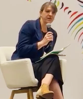 Rachel Locke sitting and holding a microphone speaking in Denver 2023