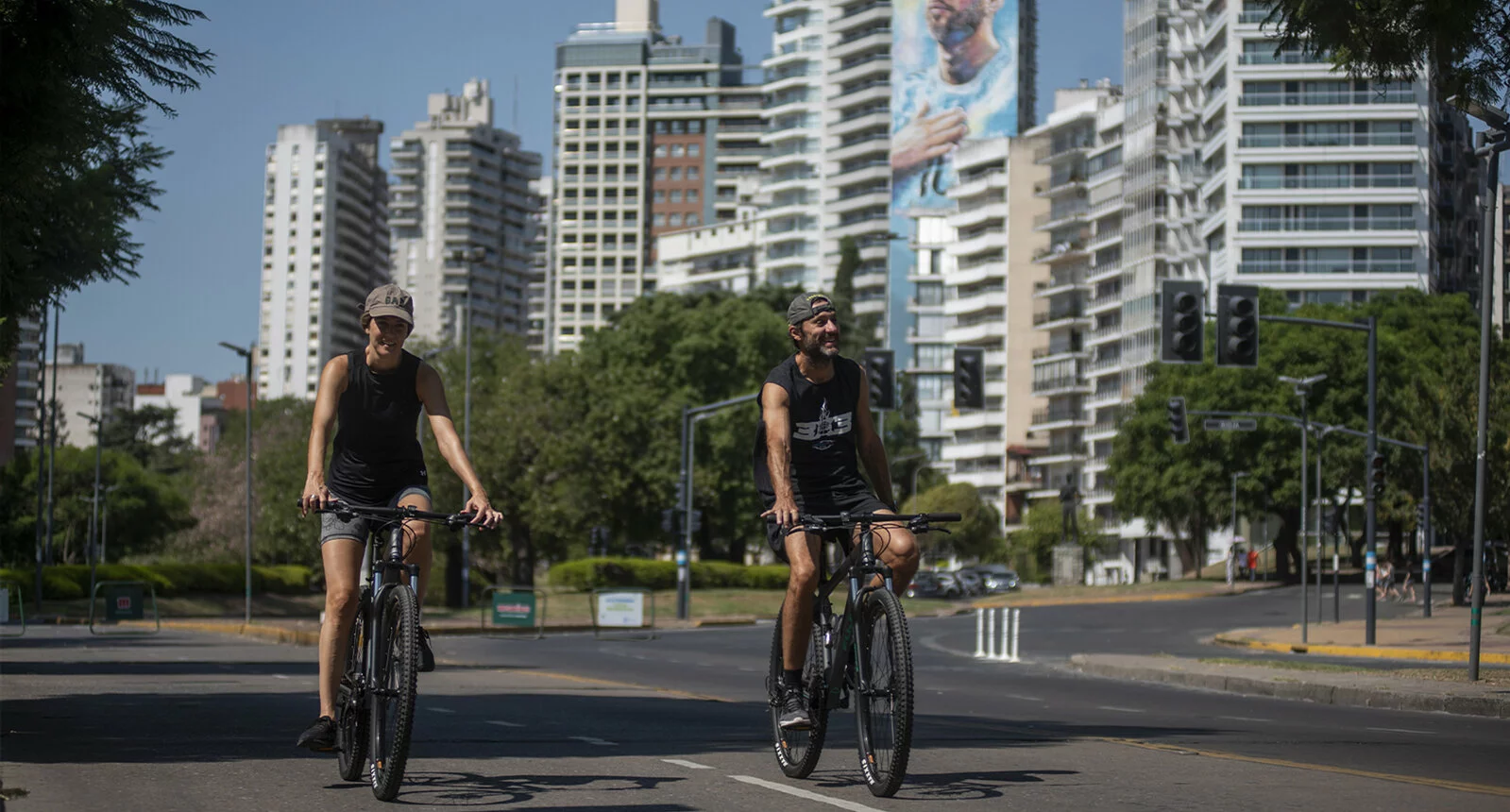 A man and a woman bike on a city street in Rosario with skyscrapers in the background.