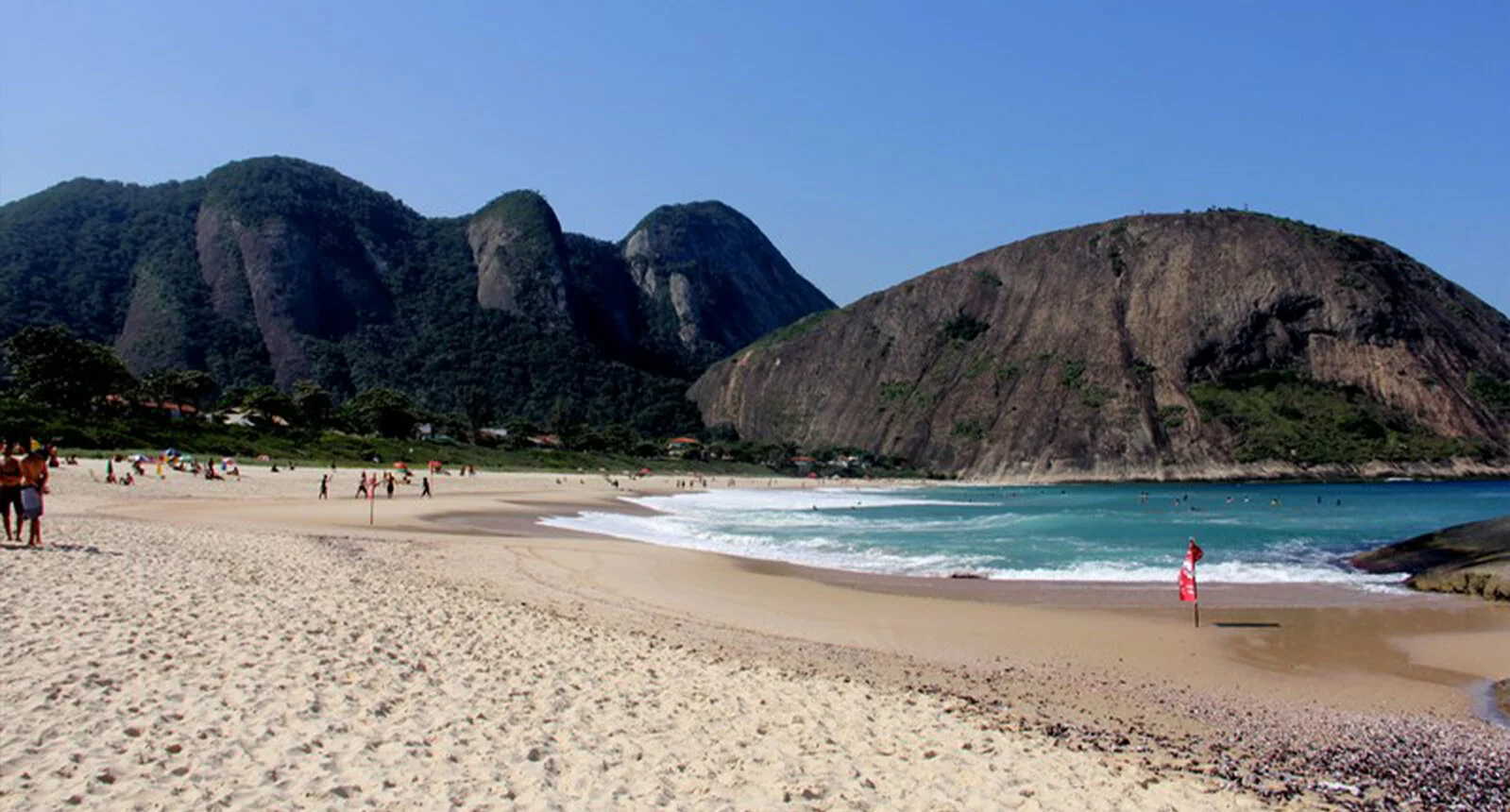 Beach with water, mountains, and people walking in Niterói